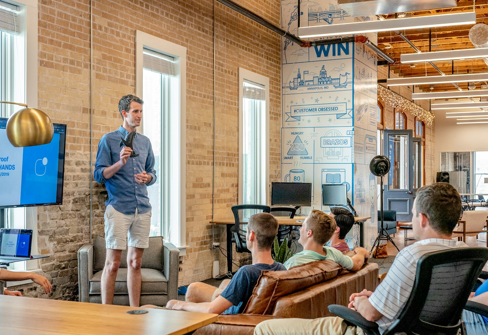 Salesforce Account Engagement Einführung mit Beyond Digital: Ein Mann präsentiert vor einem Team in einem hellen Büro mit Backsteinwand