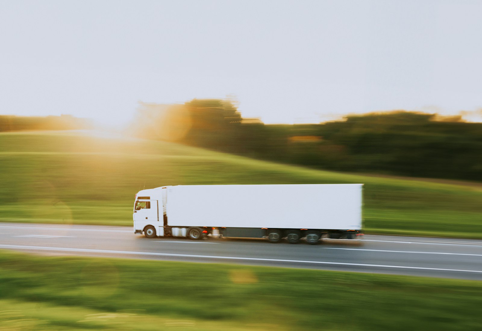 Salesforce Consumer Goods Cloud Beratung von Beyond Digital: Weißer Sattelzug fährt im Morgenlicht über eine Landstraße zwischen grünen Wiesen