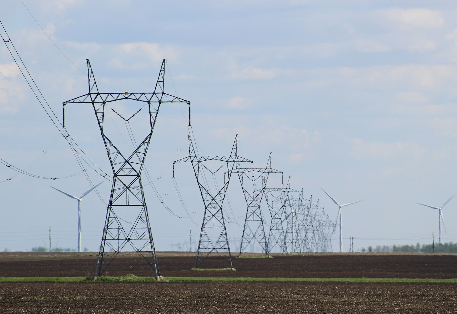 Salesforce Energy & Utilities Cloud mit Beyond Digital: Reihe von Hochspannungsmasten auf einem Feld mit Windrädern im Hintergrund
