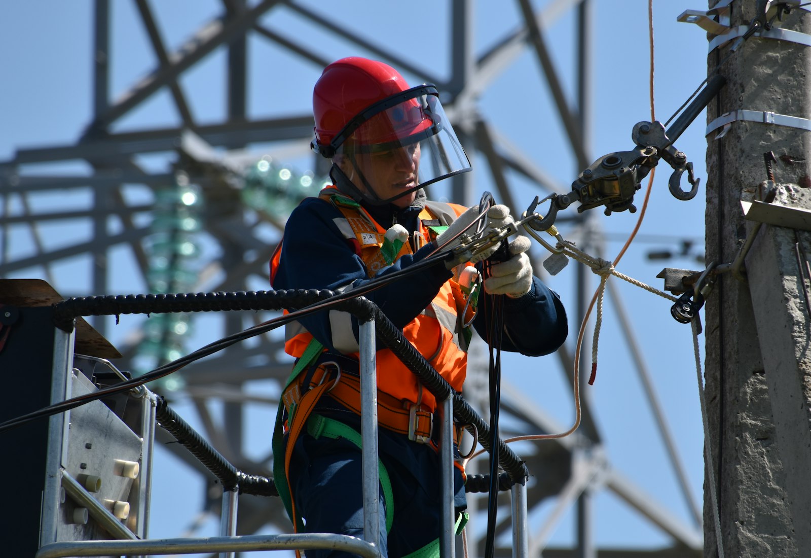 Salesforce Energy & Utilities Cloud Einführung mit Beyond Digital: Techniker mit rotem Helm und Gesichtsschutz arbeitet an einer Leitung vor einem Strommast