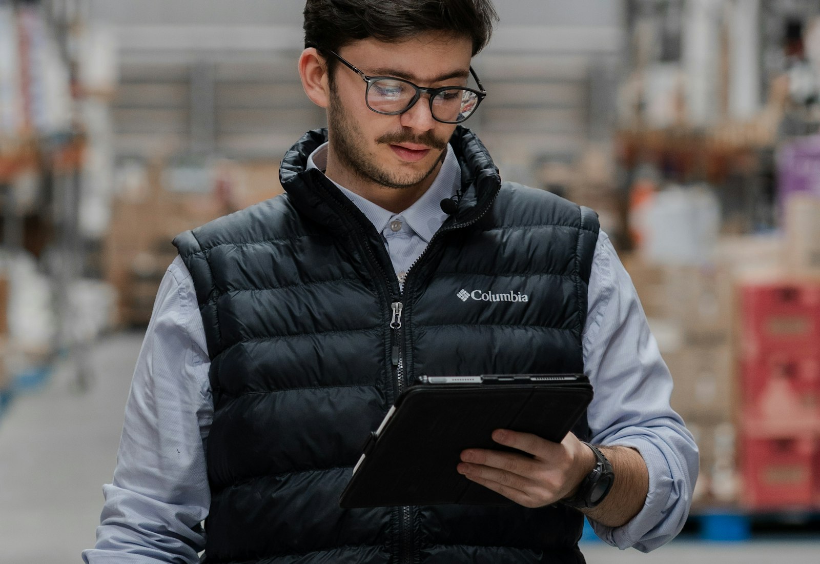 Salesforce Experience Cloud mit Beyond Digital: Mann in Weste läuft mit einem Tablet durch die Regalgänge eines Lagers