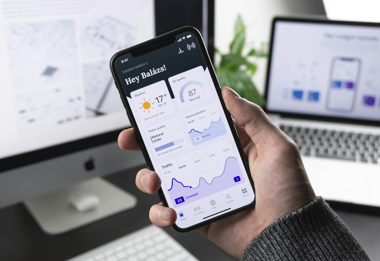 Salesforce Experience Cloud mit Beyond Digital: Hand hält ein Smartphone mit persönlicher Übersicht und Diagrammen vor einem Arbeitsplatz mit