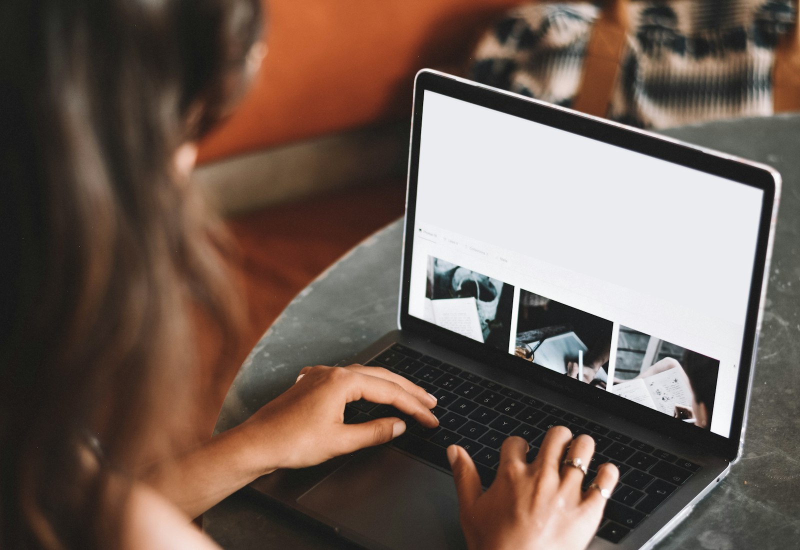 Salesforce Experience Cloud Beratung von Beyond Digital: Frau tippt an einem runden Tisch auf einem Laptop, auf dem eine Webseite mit Bildern geöffnet