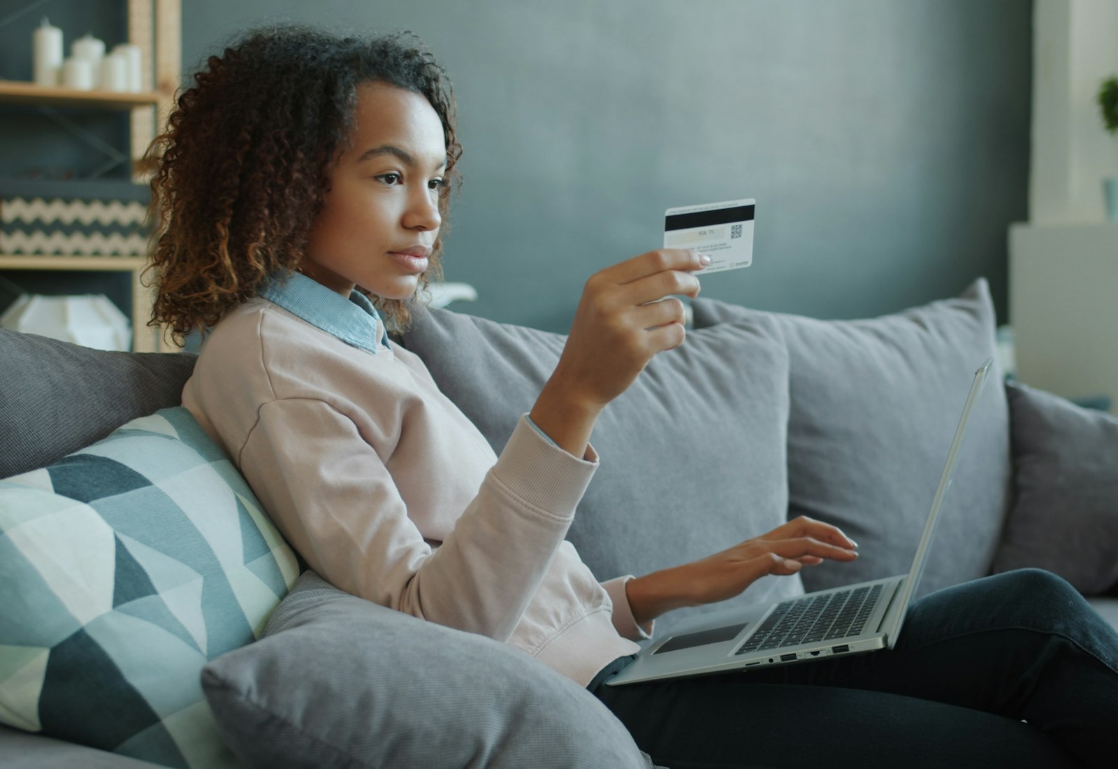 Salesforce Experience Cloud mit Beyond Digital: Frau sitzt mit Laptop und Karte in der Hand auf dem Sofa und erledigt ihr Anliegen online