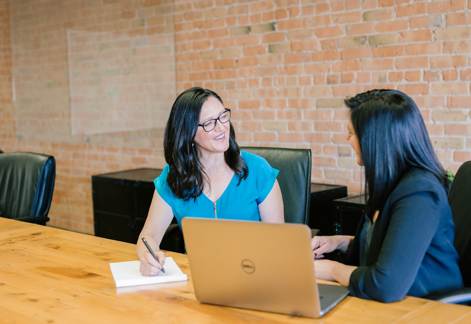 Salesforce Financial Services Cloud mit Beyond Digital: Zwei Frauen im Gespräch an einem Holztisch, eine macht Notizen, daneben ein Laptop