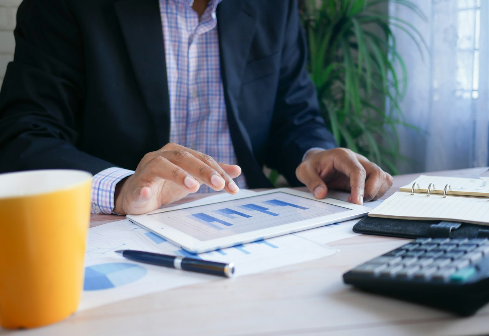 Salesforce Financial Services Cloud Beratung von Beyond Digital: Person im Anzug zeigt auf Diagramme auf einem Tablet, daneben Taschenrechner und Unterlagen