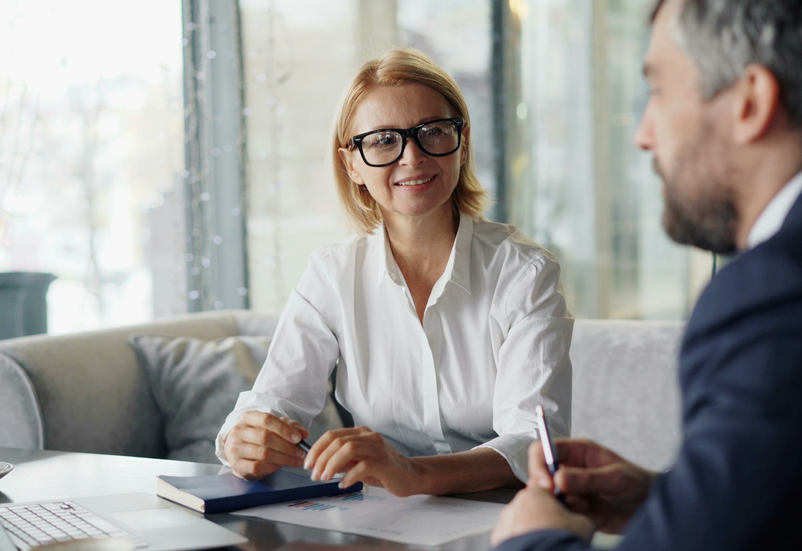 Salesforce Financial Services Cloud mit Beyond Digital: Beraterin im Gespräch mit einem Kunden an einem Tisch mit Laptop und Unterlagen