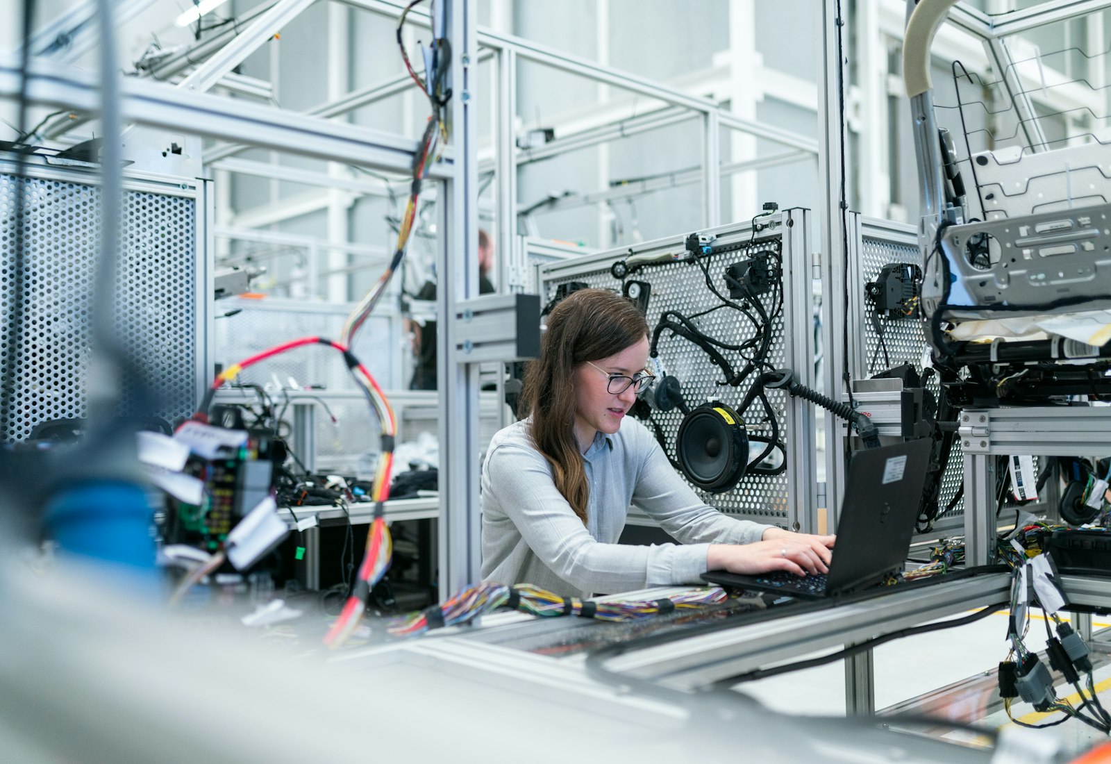 Salesforce Manufacturing Cloud mit Beyond Digital: Ingenieurin arbeitet am Laptop zwischen Prüfständen und Maschinen in einer Fertigungshalle