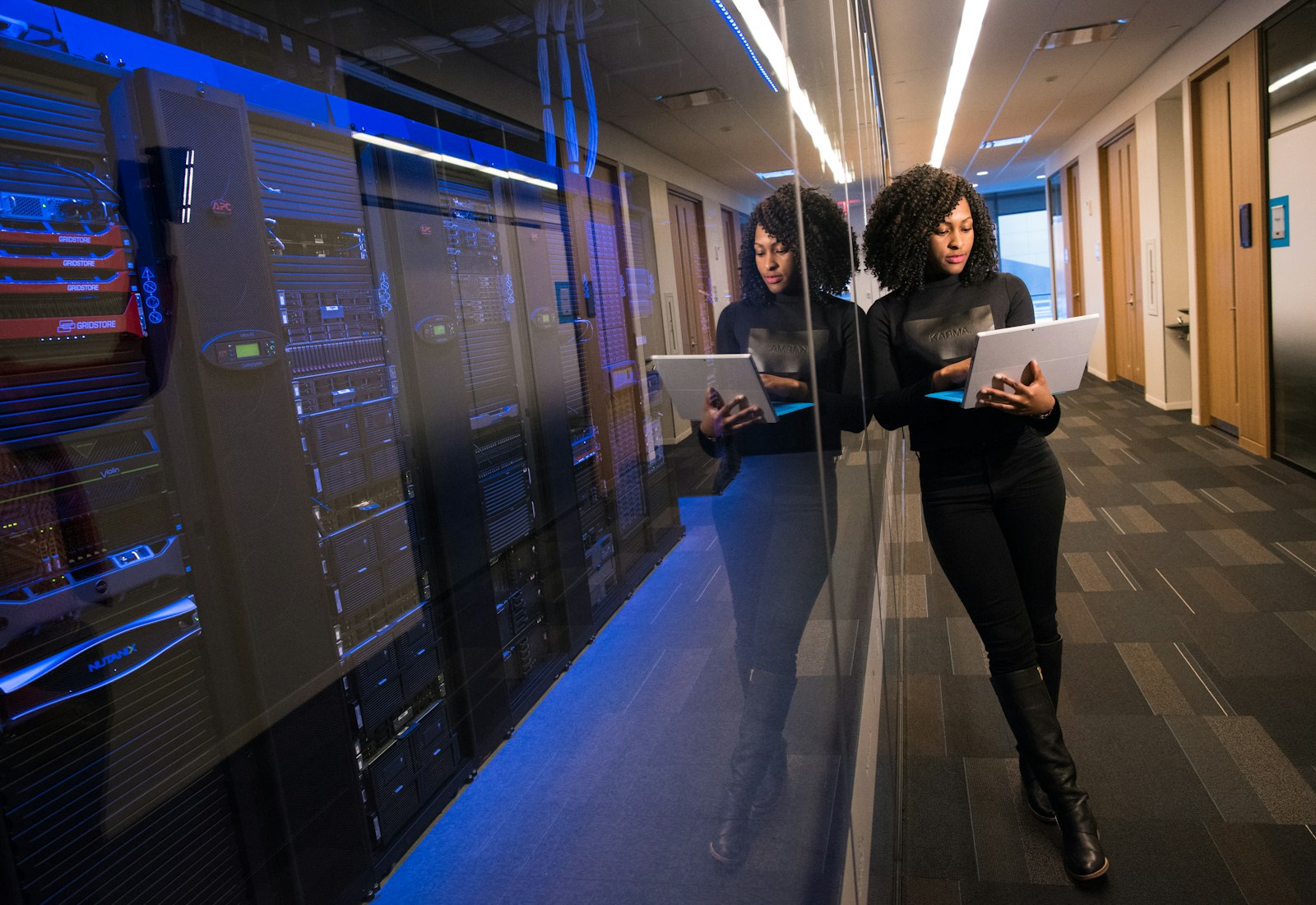 Salesforce Shield mit Beyond Digital: Zwei Fachfrauen arbeiten mit Laptop und Tablet in einem Gang neben Serverschränken