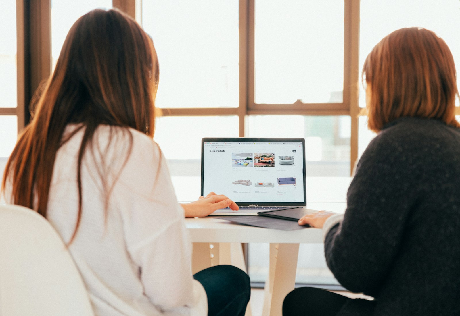 Slack Salesforce Beratung von Beyond Digital: Zwei Frauen sitzen an einem hellen Tisch am Fenster und besprechen sich vor einem Laptop