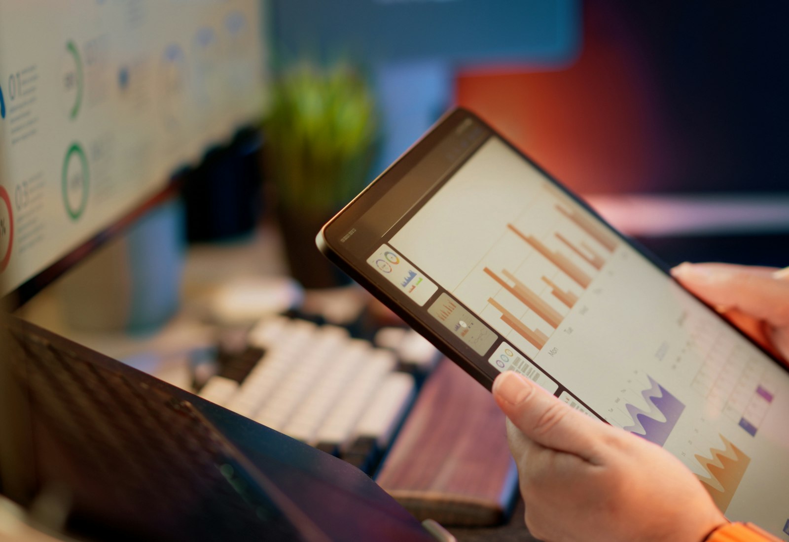 Tableau Salesforce mit Beyond Digital: Hände halten ein Tablet mit Balkendiagrammen vor einem Arbeitsplatz mit Monitor und Tastatur